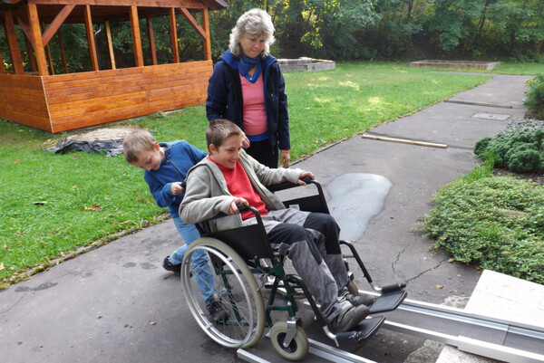 Žáci na invalidním vozíku překonávají pomocí ližin 2 schody u vstupu do Denního stacionáře